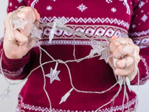 Woman in red holiday sweater holding tangled holiday lights